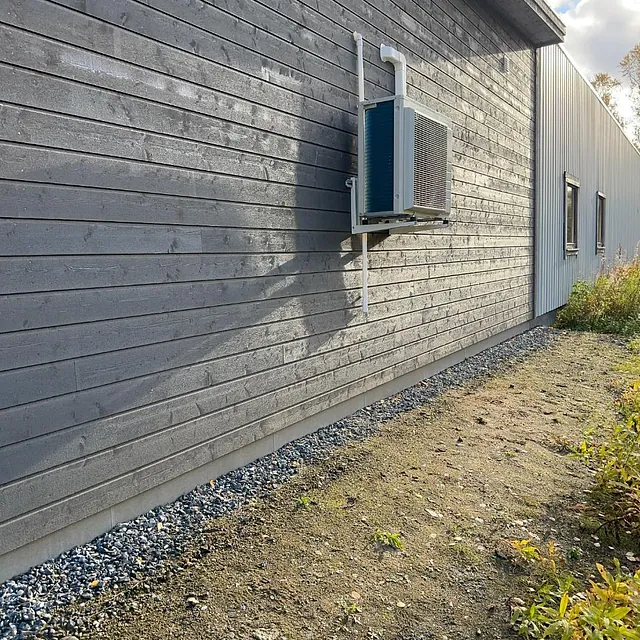 Utedel av varmepumpe montert på grå husvegg