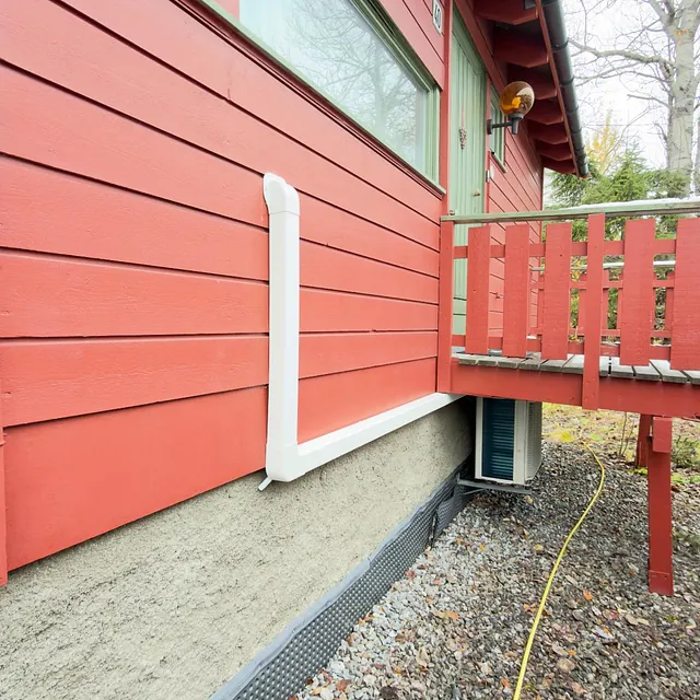 Utedel av varmepumpe montert på rød trekledning ved husvegg