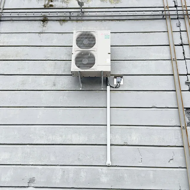 Utedel av varmepumpe montert på grå vegg med vertikale bord