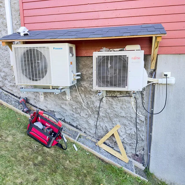 To varmepumpe utedeler montert på mur under rød trekledning