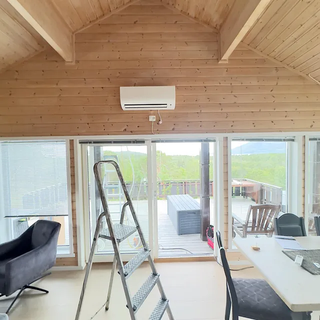 Varmepumpe montert høyt oppe på vegg i rom med skråtak og spisebord