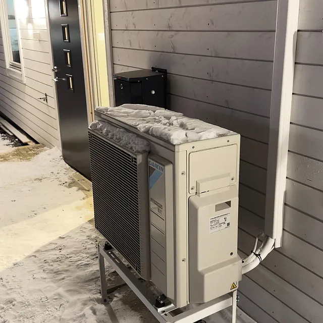 Utedel av varmepumpe på stativ ved husvegg i en inngangssone