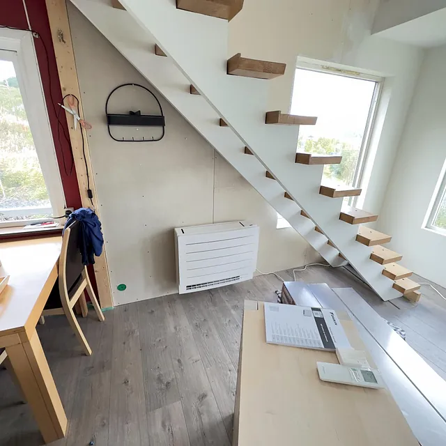 Moderne stue med varmepumpe montert på veggen under trapp