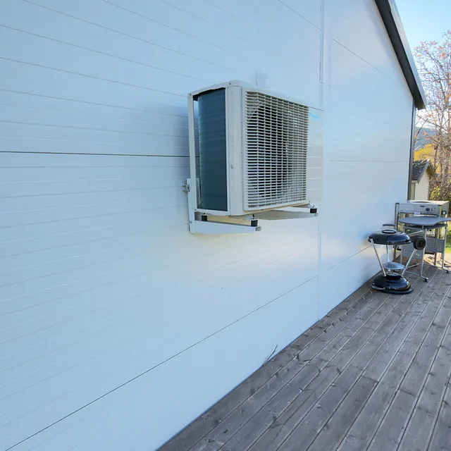 Utedel av varmepumpe montert på hvit kledning på terrasse